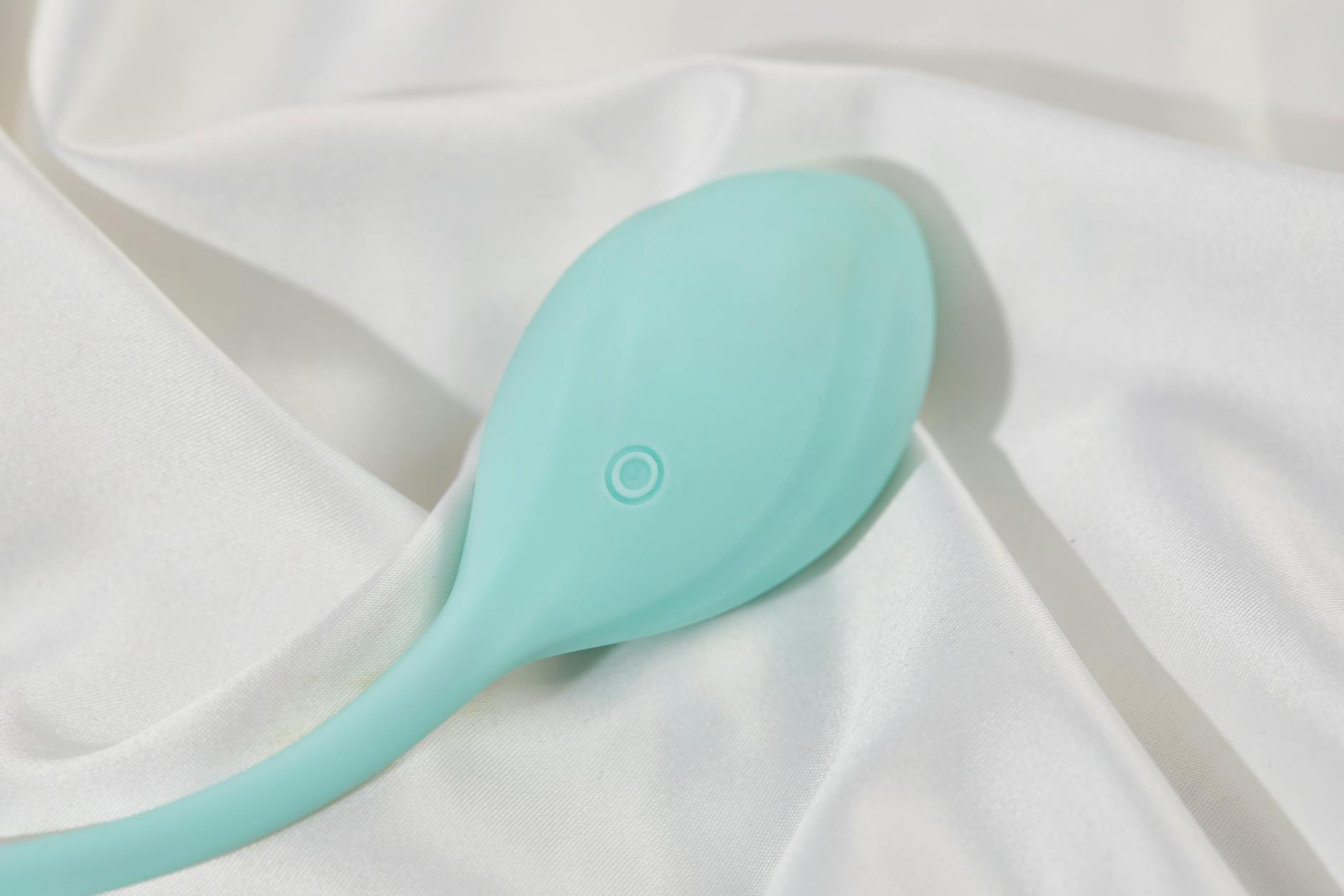 A teal silicone clitoral vibrator resting on smooth white fabric, symbolizing modern sexual wellness