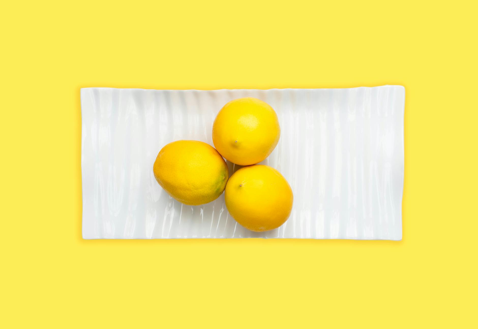 A hand holding a lemon-colored vibrator against a minimalist purple background