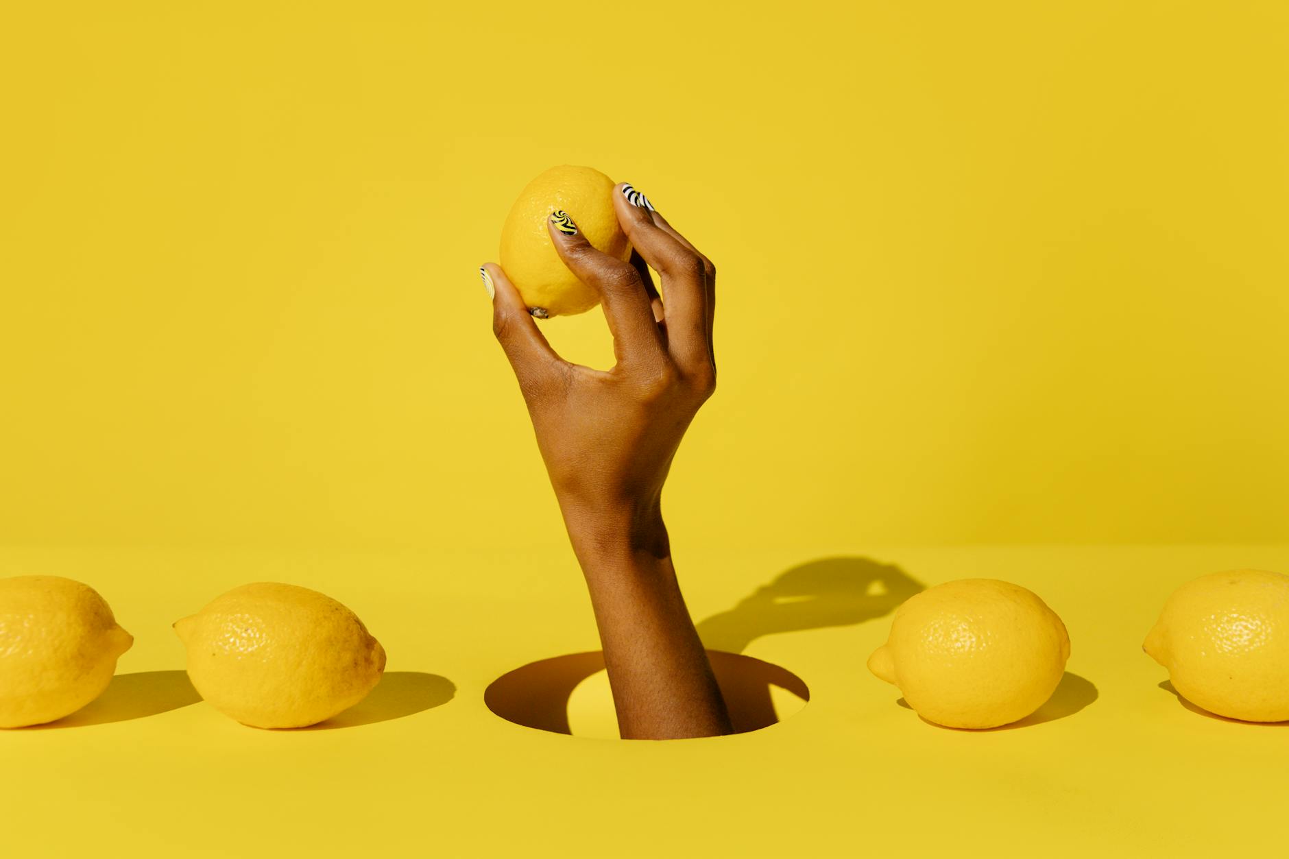 Hand holding a lemon against a bright yellow background, symbolizing fresh approaches to pleasure