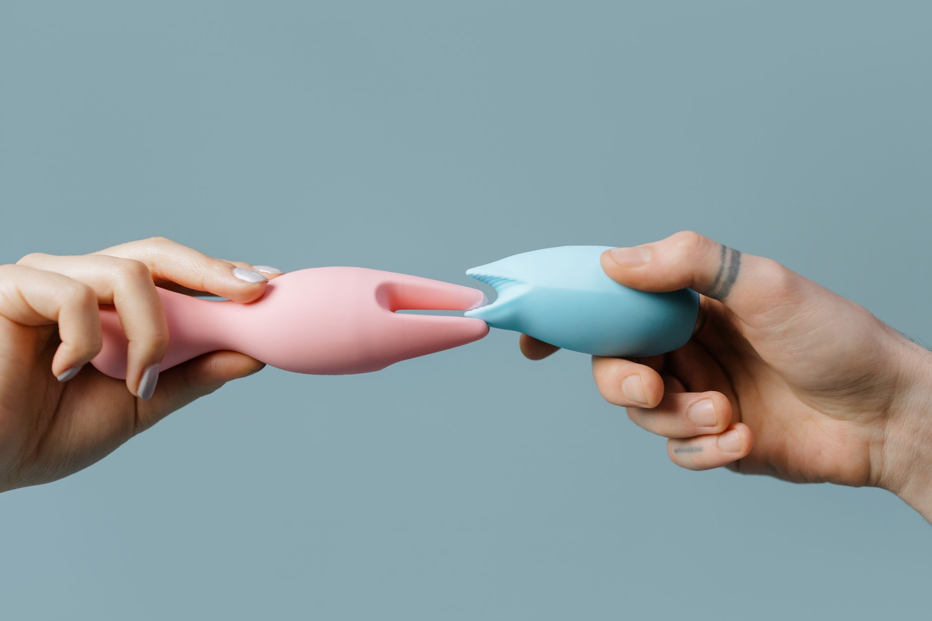 Hands holding colorful silicone vibrators against a pastel background