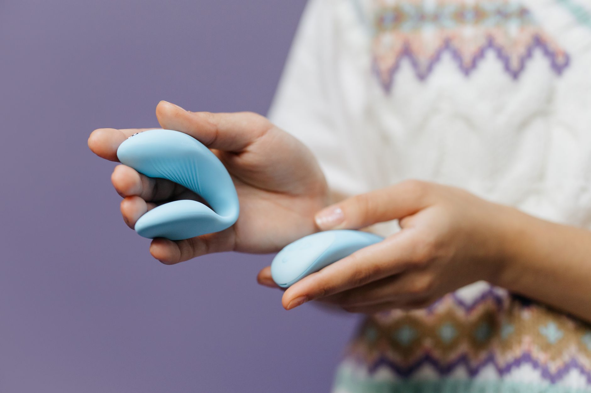 Close-up of hands holding a sleek vibrator against a purple background, representing first-time toy exploration.