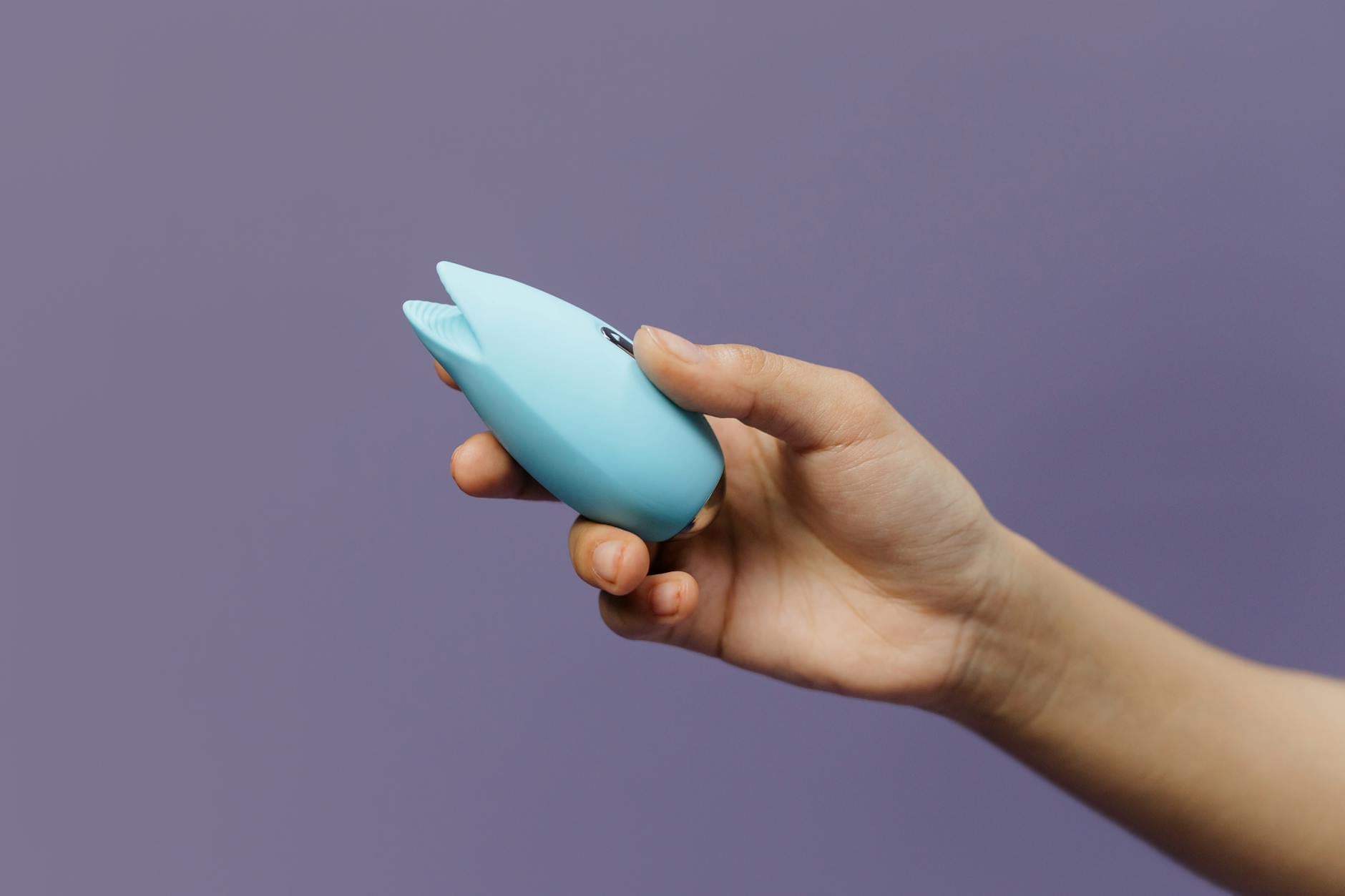 A blue silicone lemon vibrator held in hand against a purple background