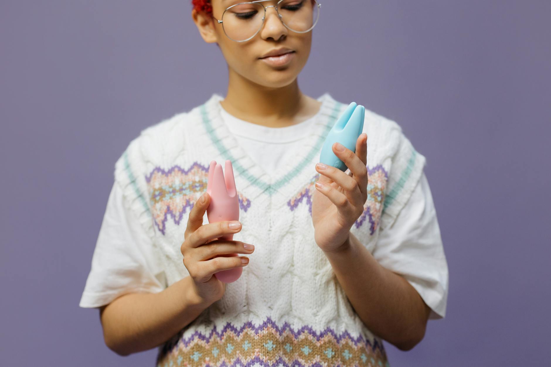 Woman holding blue and pink silicone vibrators in a contemplative, centered manner.